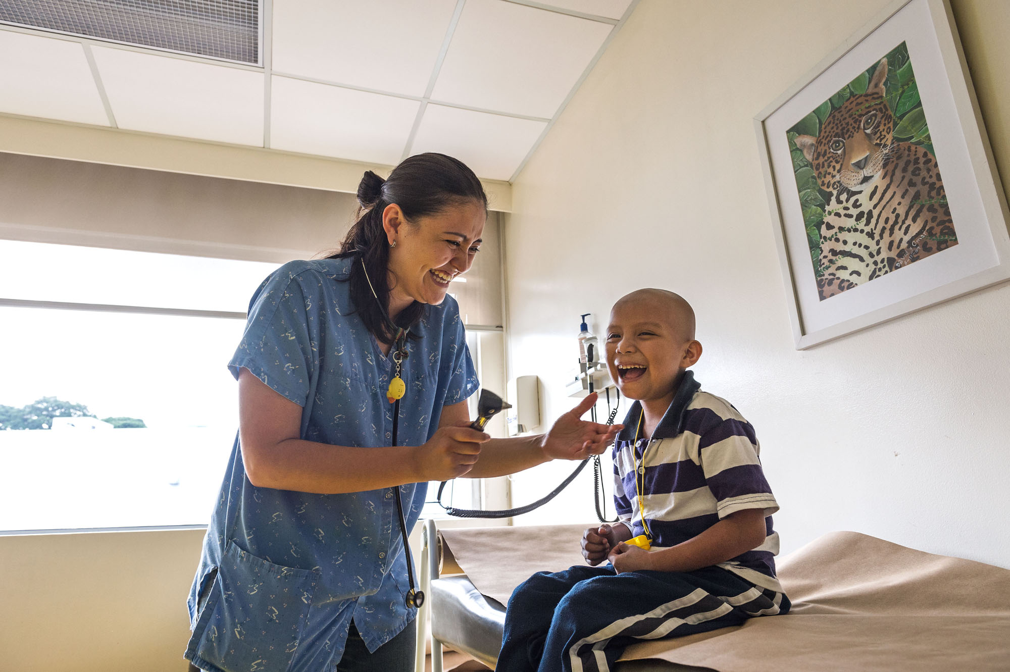 A female health care worker is examining a smiling happpy boy who's sitting on a hospital bed.