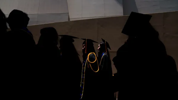Graduates wearing caps and gowns exit a graduation ceremony.