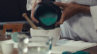 a person pours green powder into a mortar