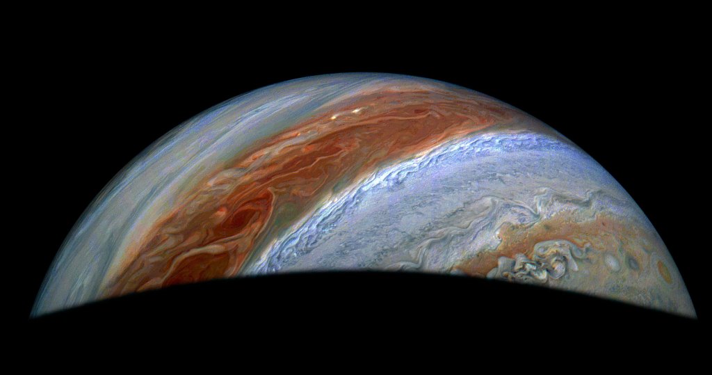 Enhanced-color image of Jupiter’s northern hemisphere, captured by NASA’s Juno spacecraft, showing swirling clouds and storm bands in vivid red, orange, and blue tones.